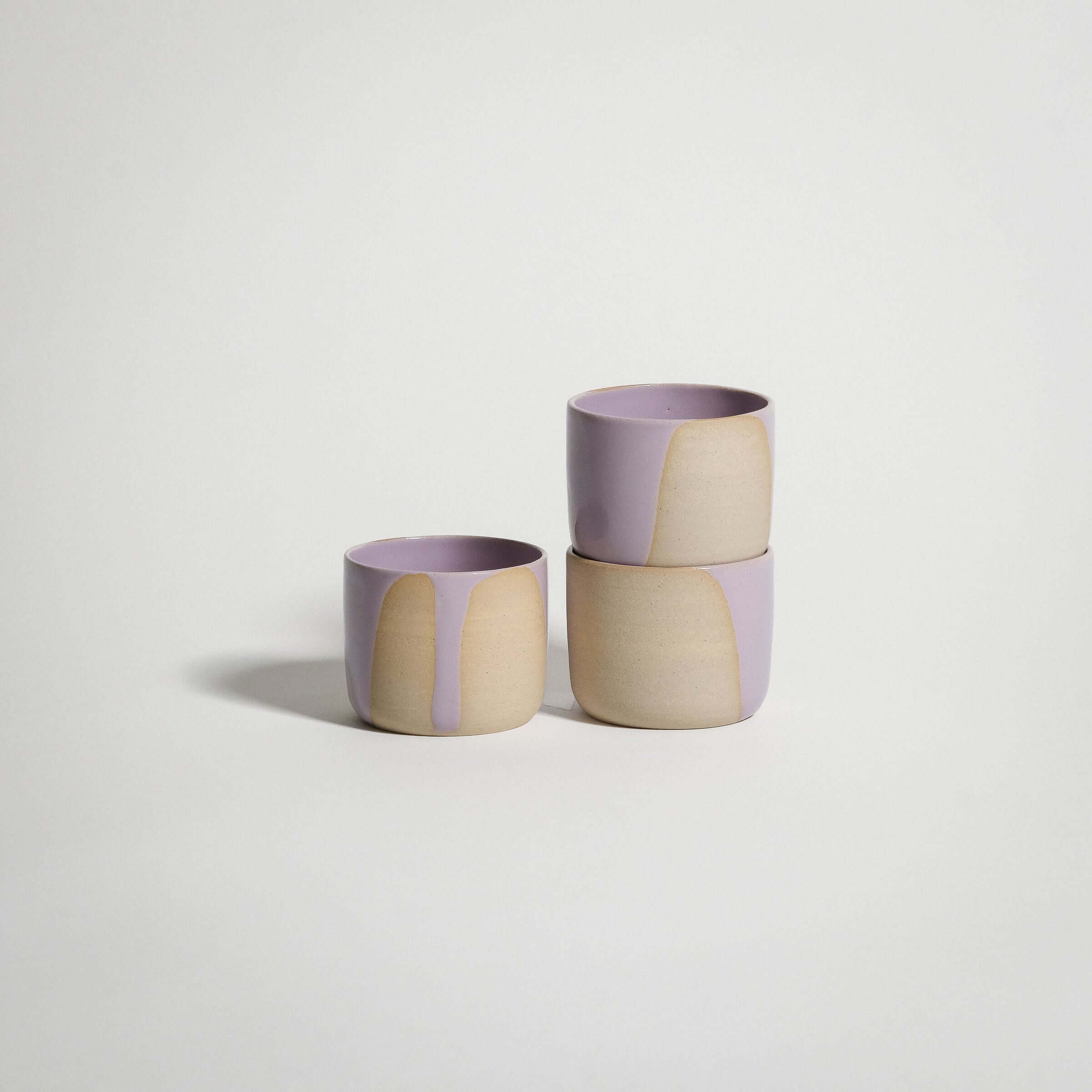 Handcrafted lilac and beige espresso cups stacked, showcasing unique glaze patterns on stoneware clay.