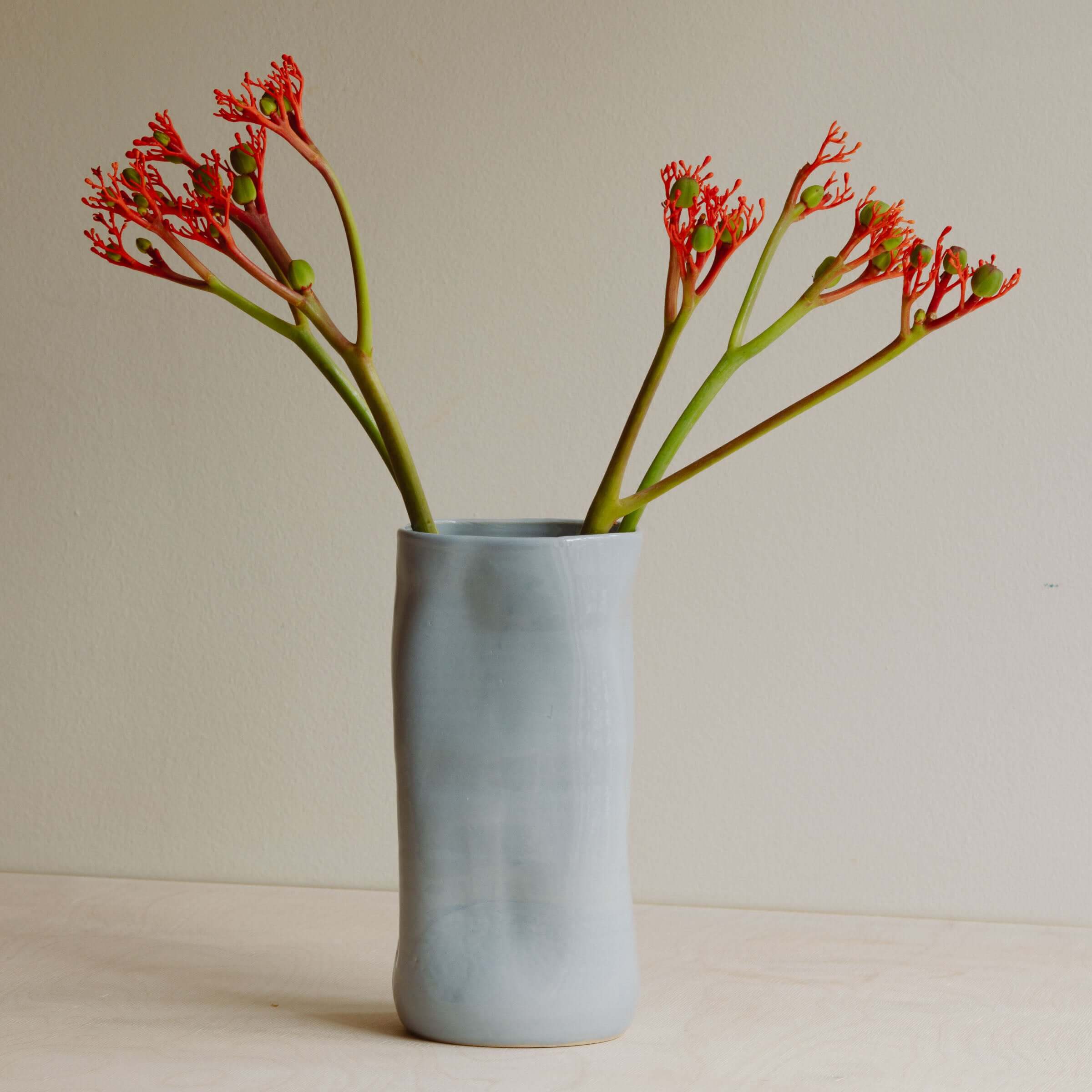 Handcrafted ice-blue stoneware vase holding vibrant red flowers, showcasing unique texture and color variations.