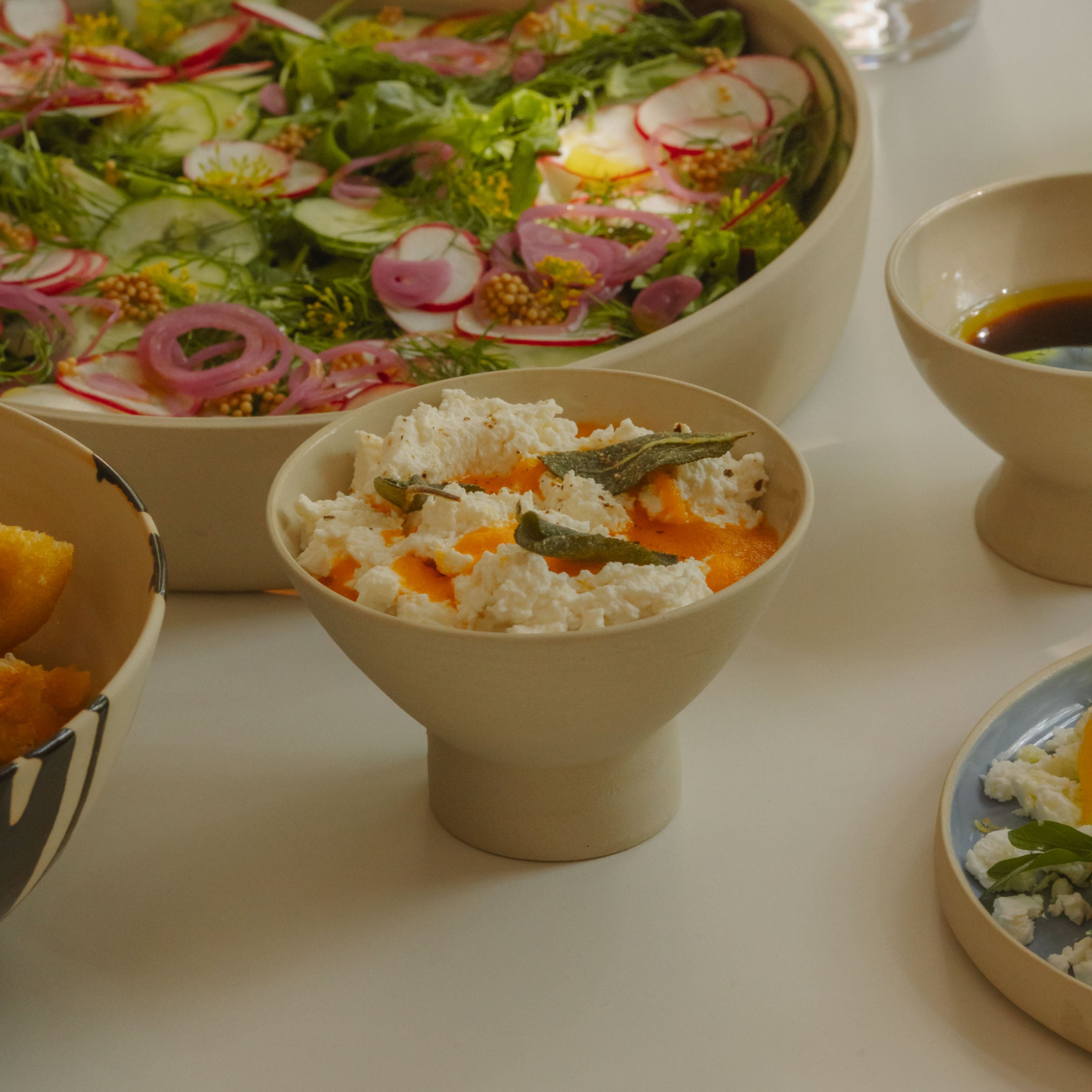 Small matte dessert bowl filled with creamy dish, surrounded by colorful salad and side dishes on a dining table.