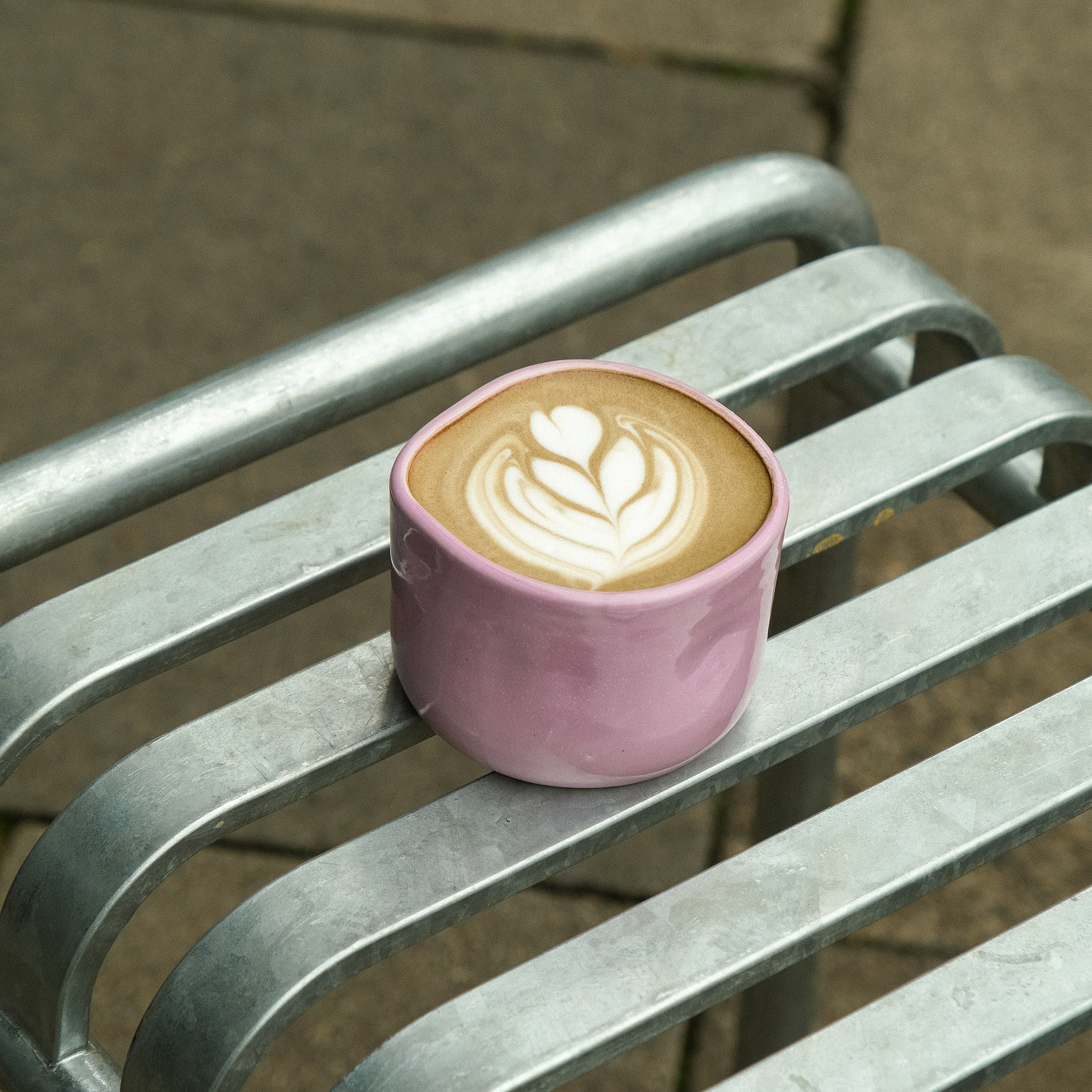 Hojicha Cup – Pink placed on a metal chair, featuring a latte art design on top.