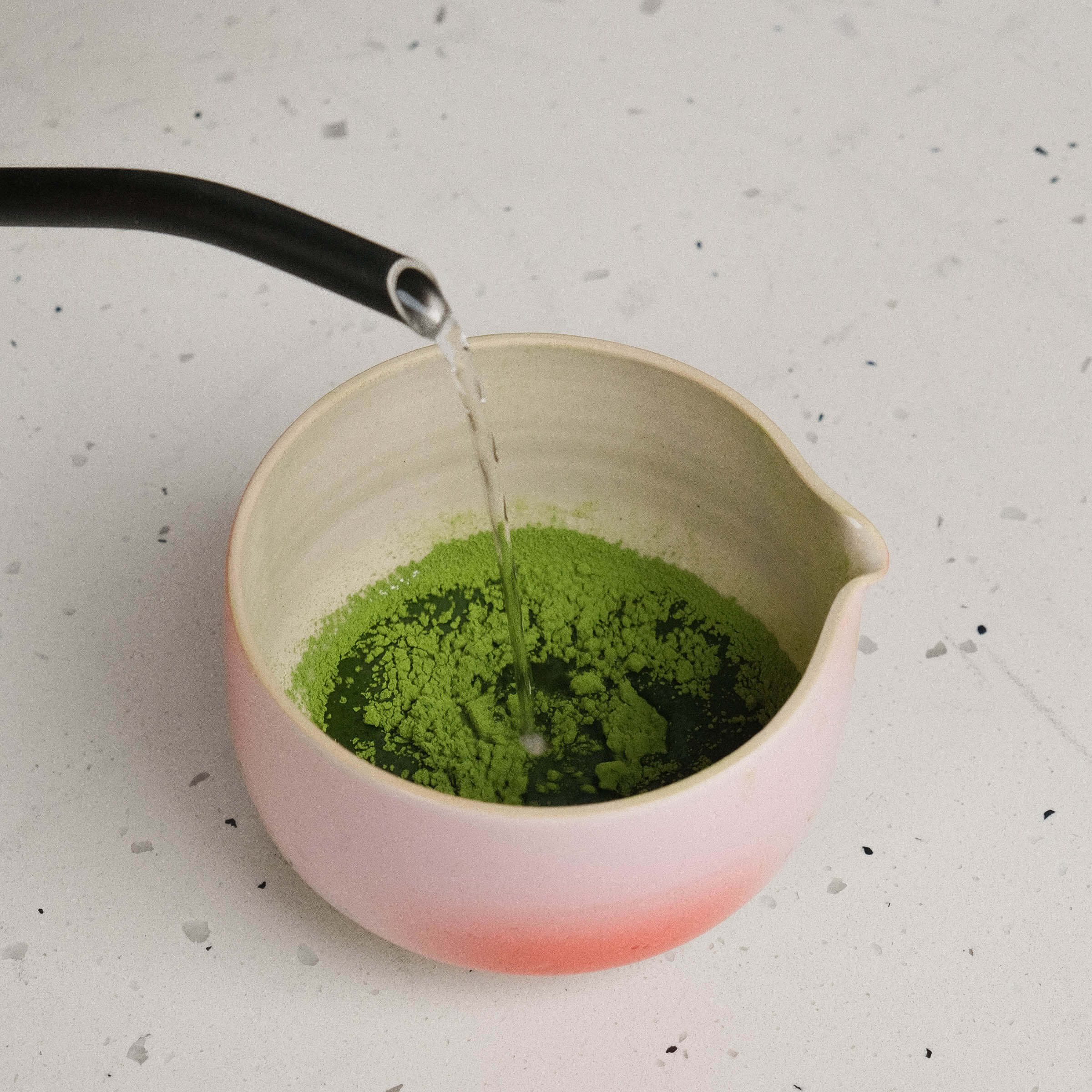 Pouring hot water into a bowl of organic ceremonial matcha powder, showcasing vibrant green color.