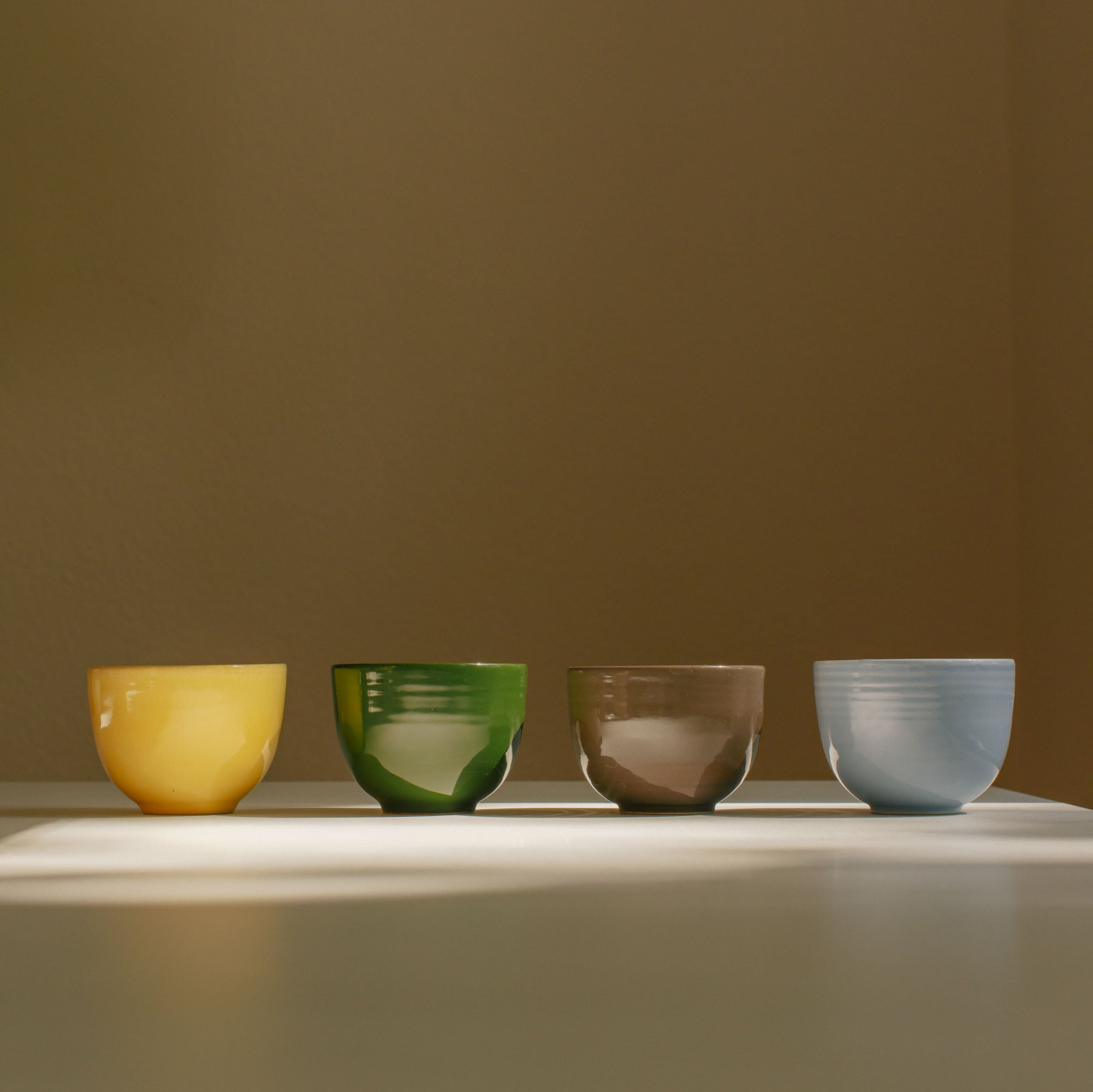 Set of 4 handcrafted stoneware coffee cups in yellow, green, brown, and ice blue, highlighting ceramic beauty.