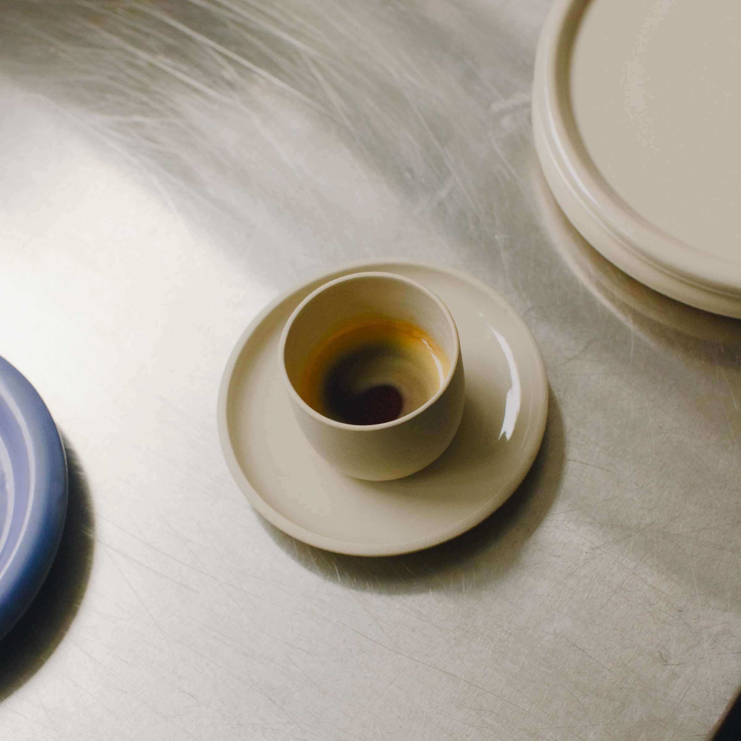 Set of 4 Nomi Creme espresso cups in grey stoneware with glossy glaze, featured on a metal surface.