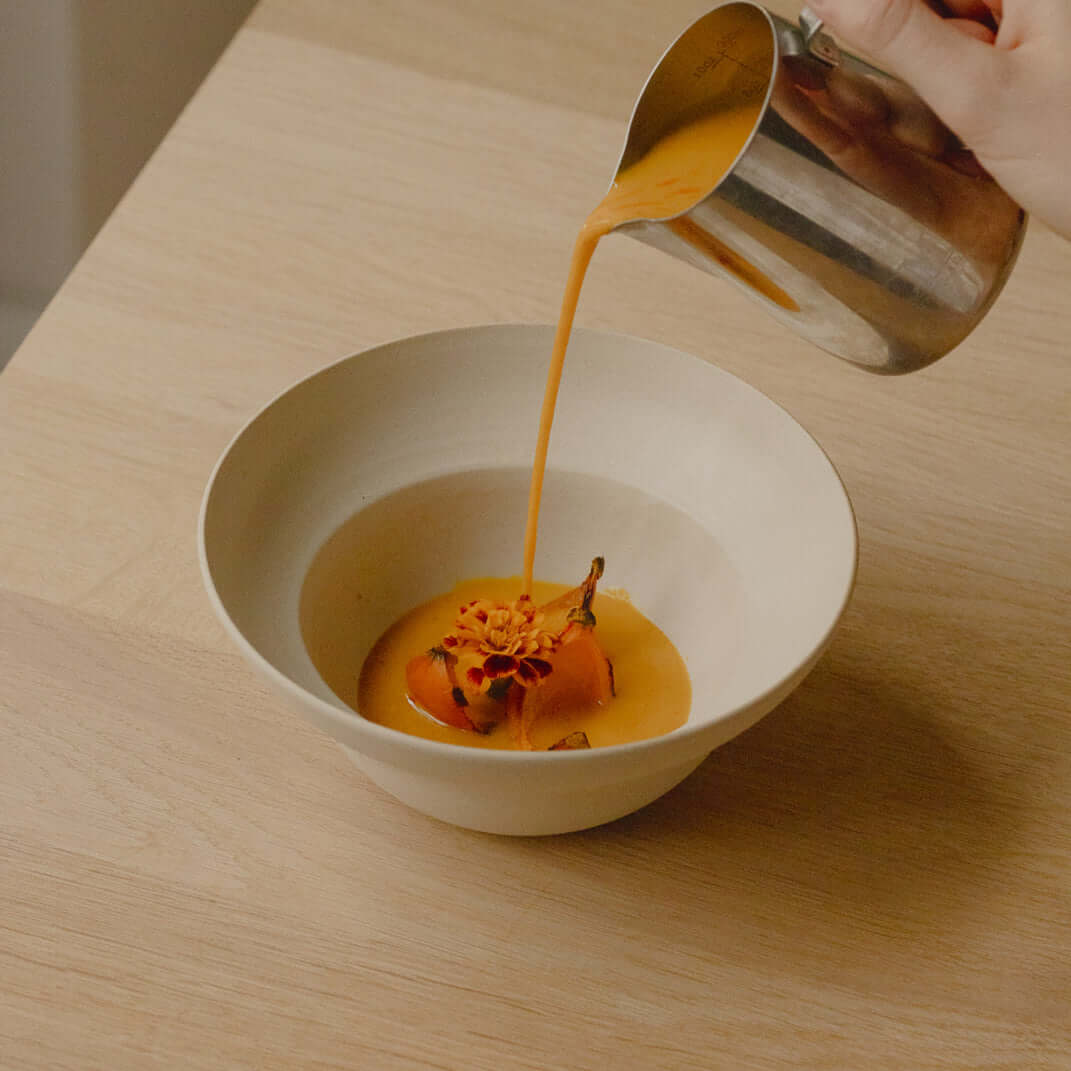 Set of 4 Neo Bowls in White Matte with soup being poured into one on a wooden table.