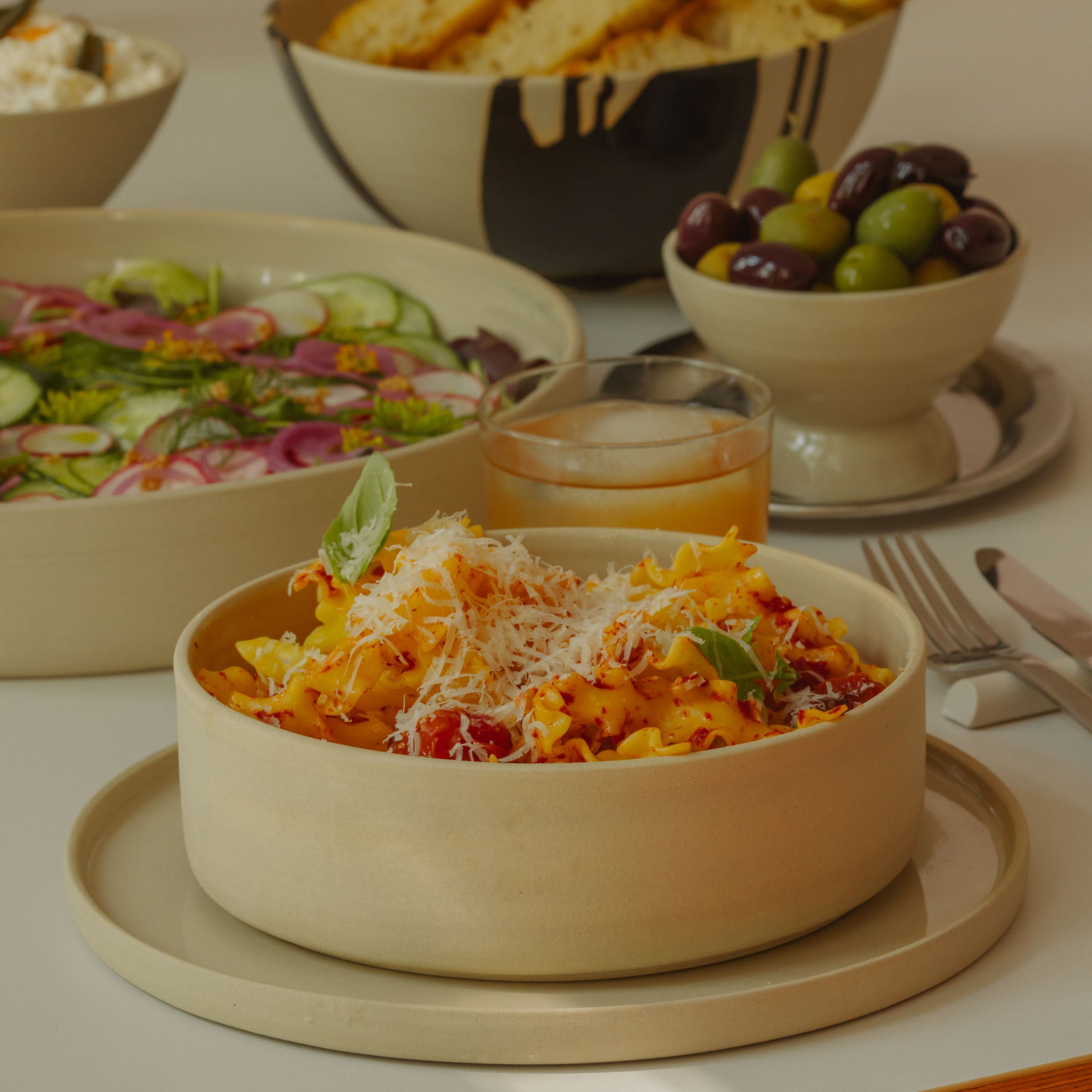 Set of 4 Nomi Creme Pasta Bowls with pasta, salad, and olives, showcasing a modern table setting.