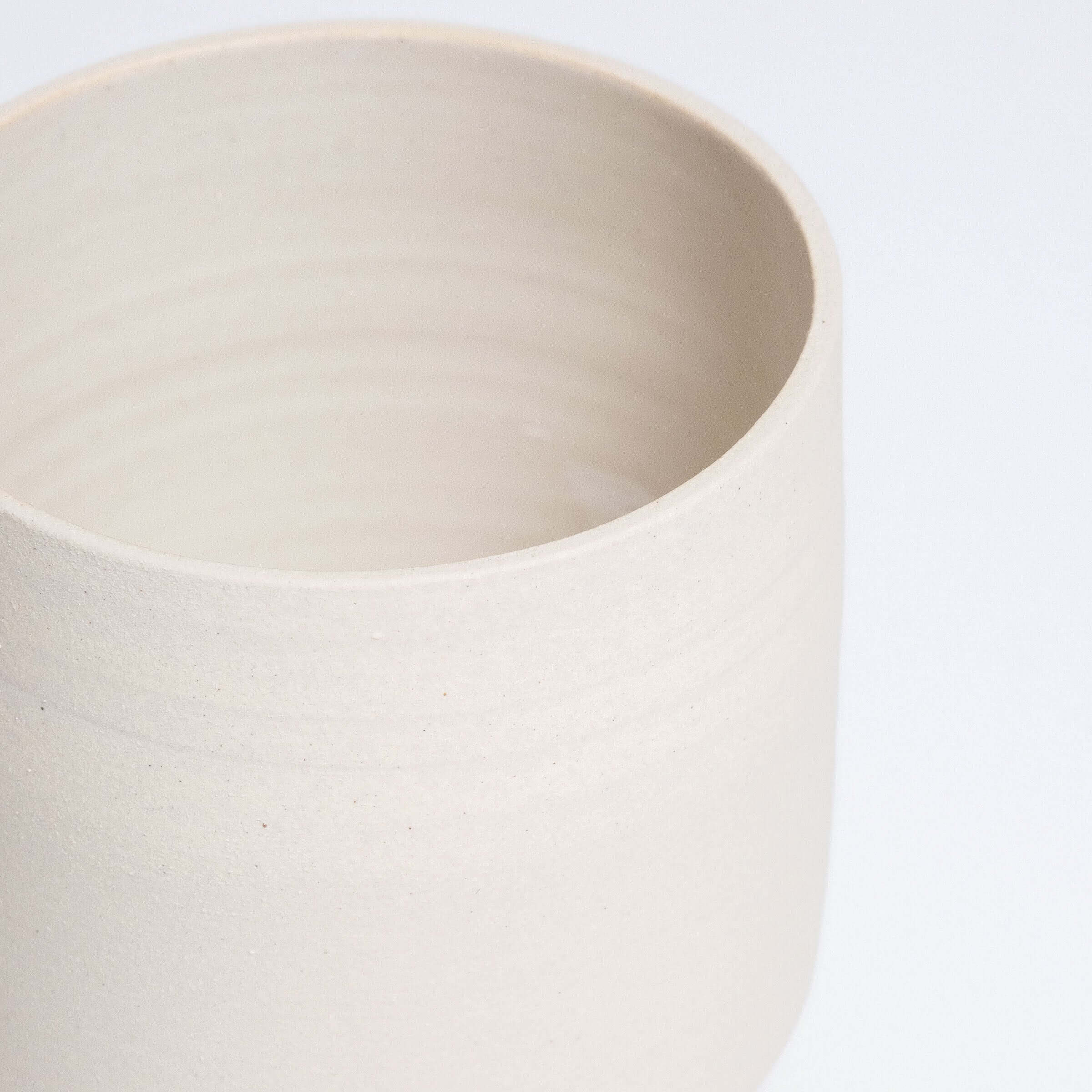 Close-up of a simple beige stoneware tea cup, featuring a smooth, glossy interior and raw exterior finish.