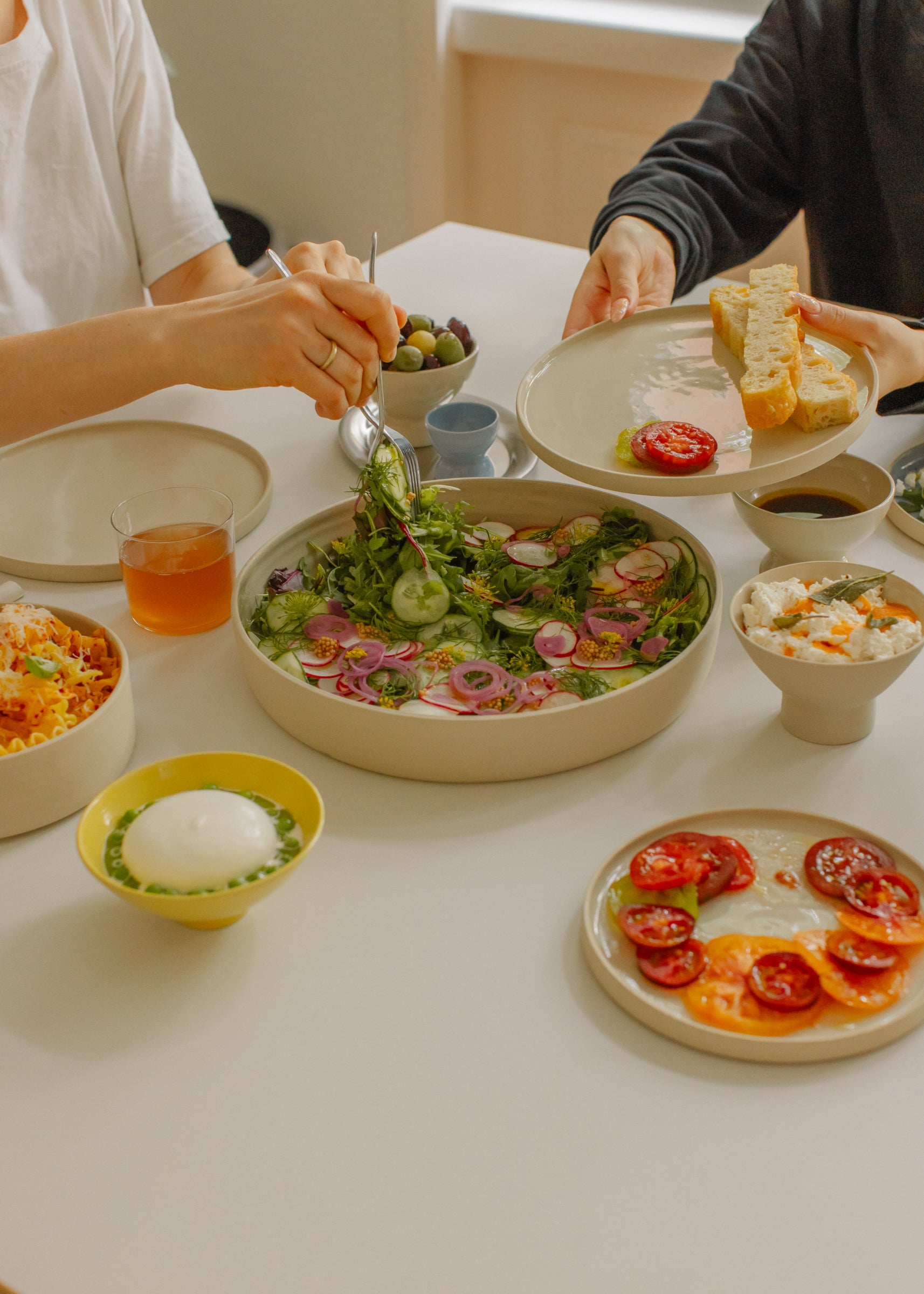 A beautifully arranged table with plates of fresh salads, bread, and desserts showcasing timeless ceramics from the Core Collection.