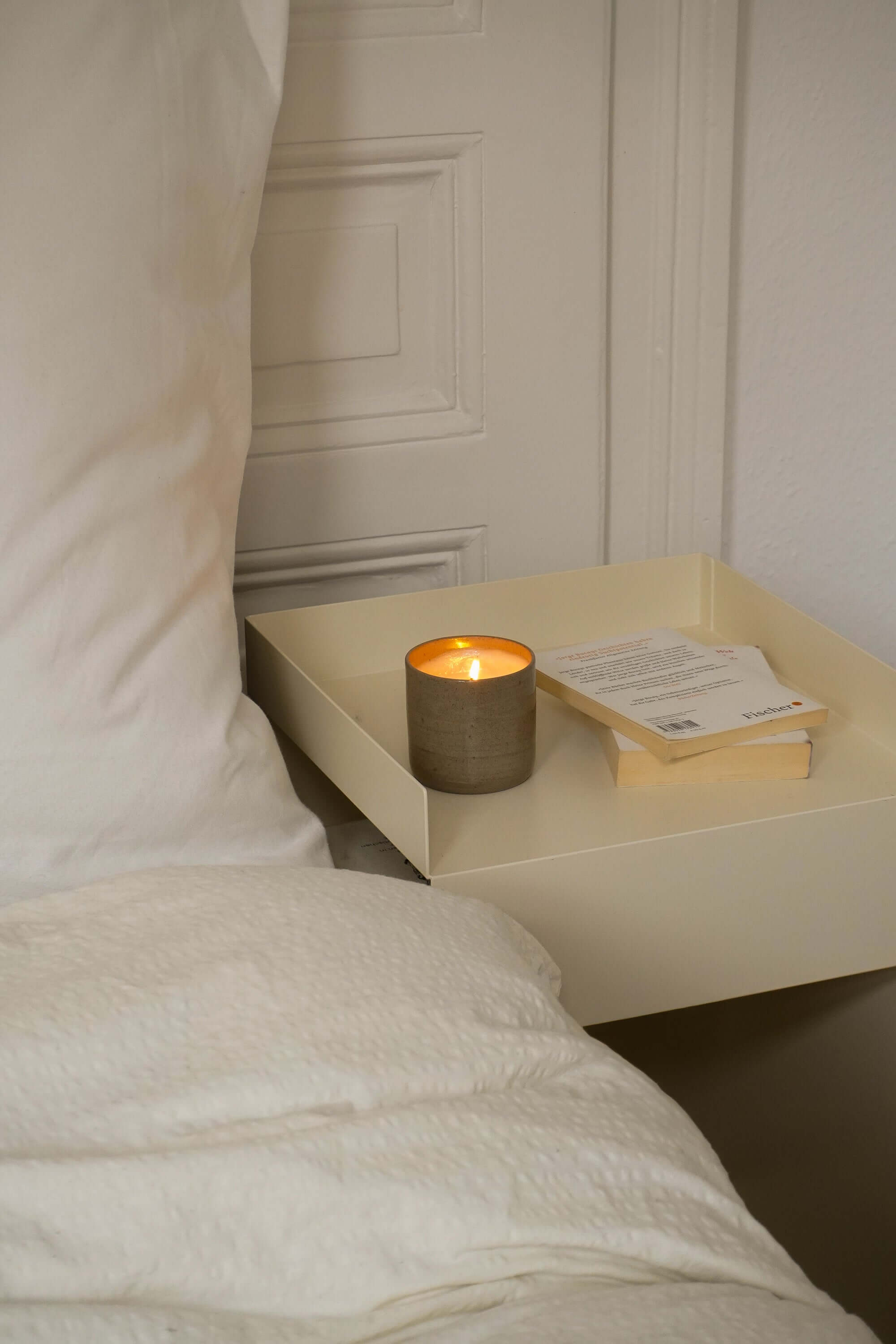 Herbstliche Duftkerzen auf einem Nachttisch, umgeben von einem gemütlichen Bett und einem Buch.