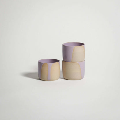 Handcrafted lilac and beige espresso cups stacked, showcasing unique glaze patterns on stoneware clay.