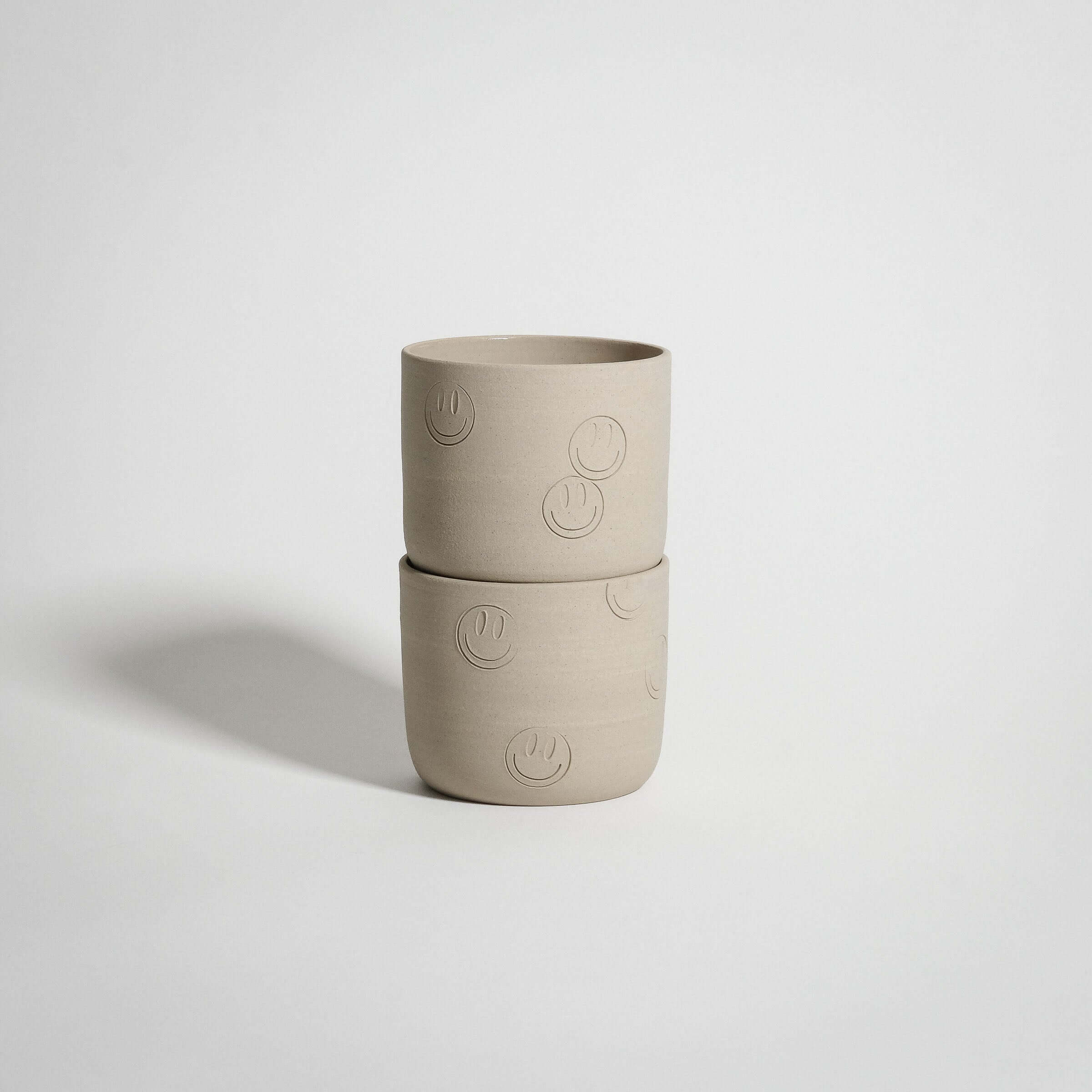 Stacked smiley coffee cup in grey stoneware with playful embossed smiley faces.
