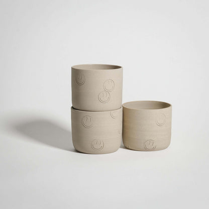 Three wheel-thrown stoneware cups with smiley face stamps, light grey color, perfect for beverages.