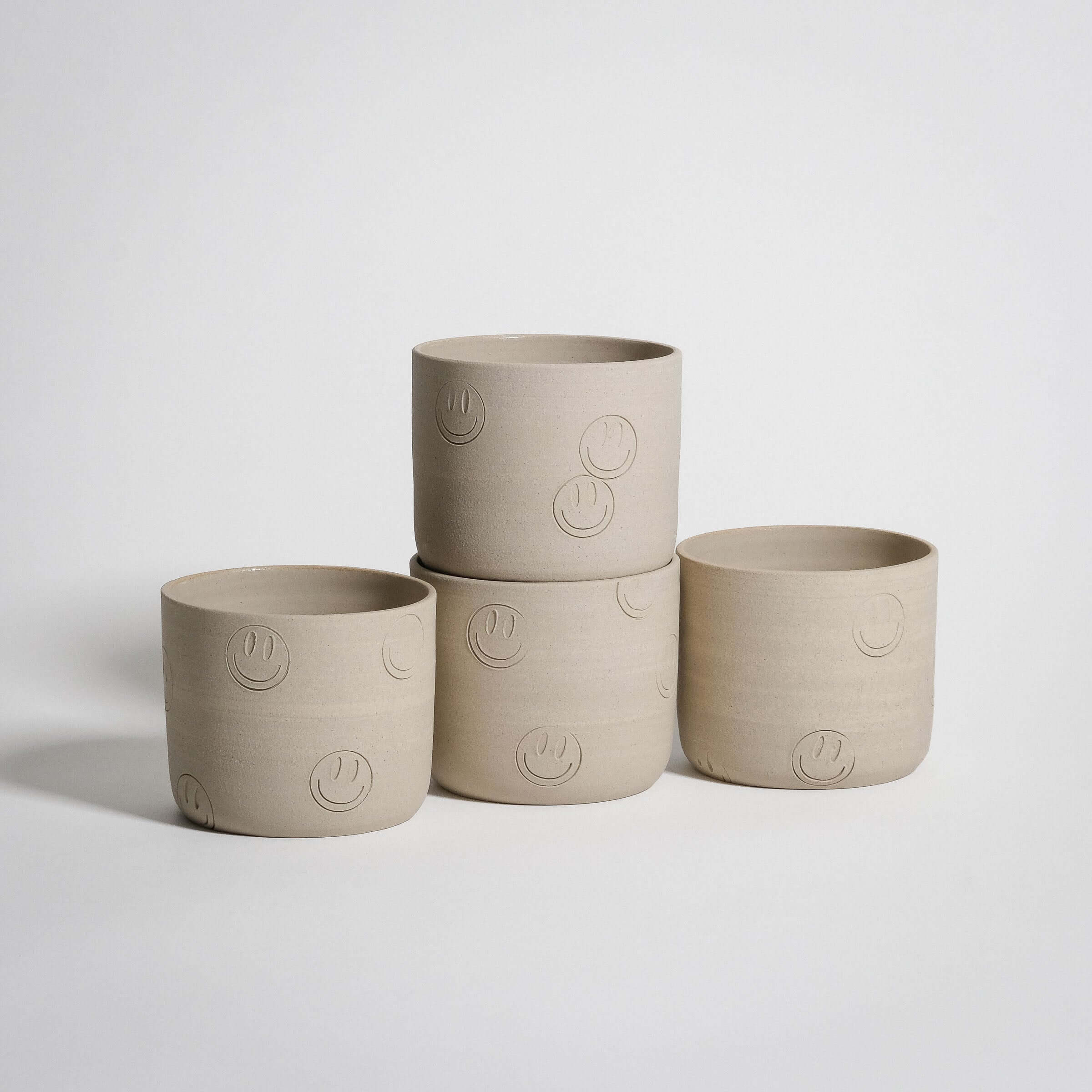 Smiley coffee cup set made of grey stoneware with stamped smiley faces, featuring four handcrafted wheel-thrown pieces.