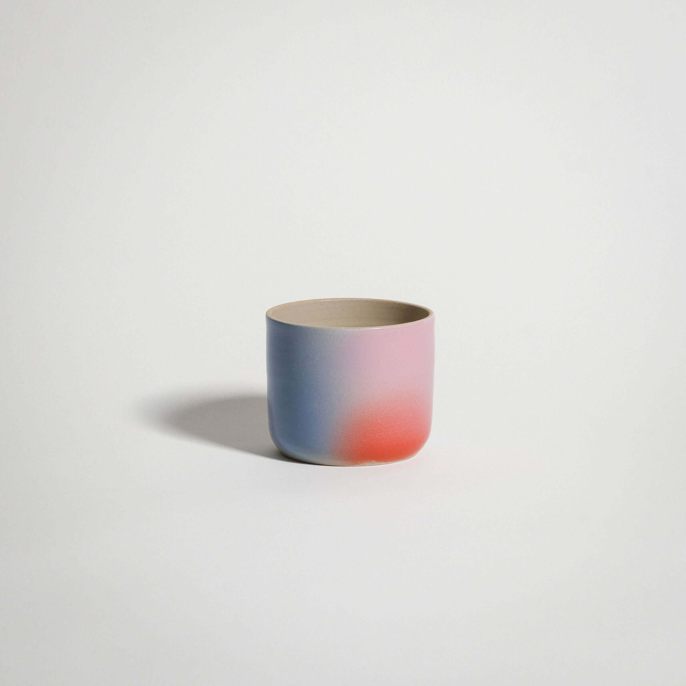 Dawn Coffee Cup, handcrafted grey stoneware with glossy glaze and gradient colors of red, blue, and lilac.