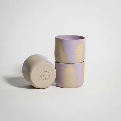 Handcrafted wheel-thrown stoneware coffee cups with glossy lilac and pink glazes, stacked elegantly.