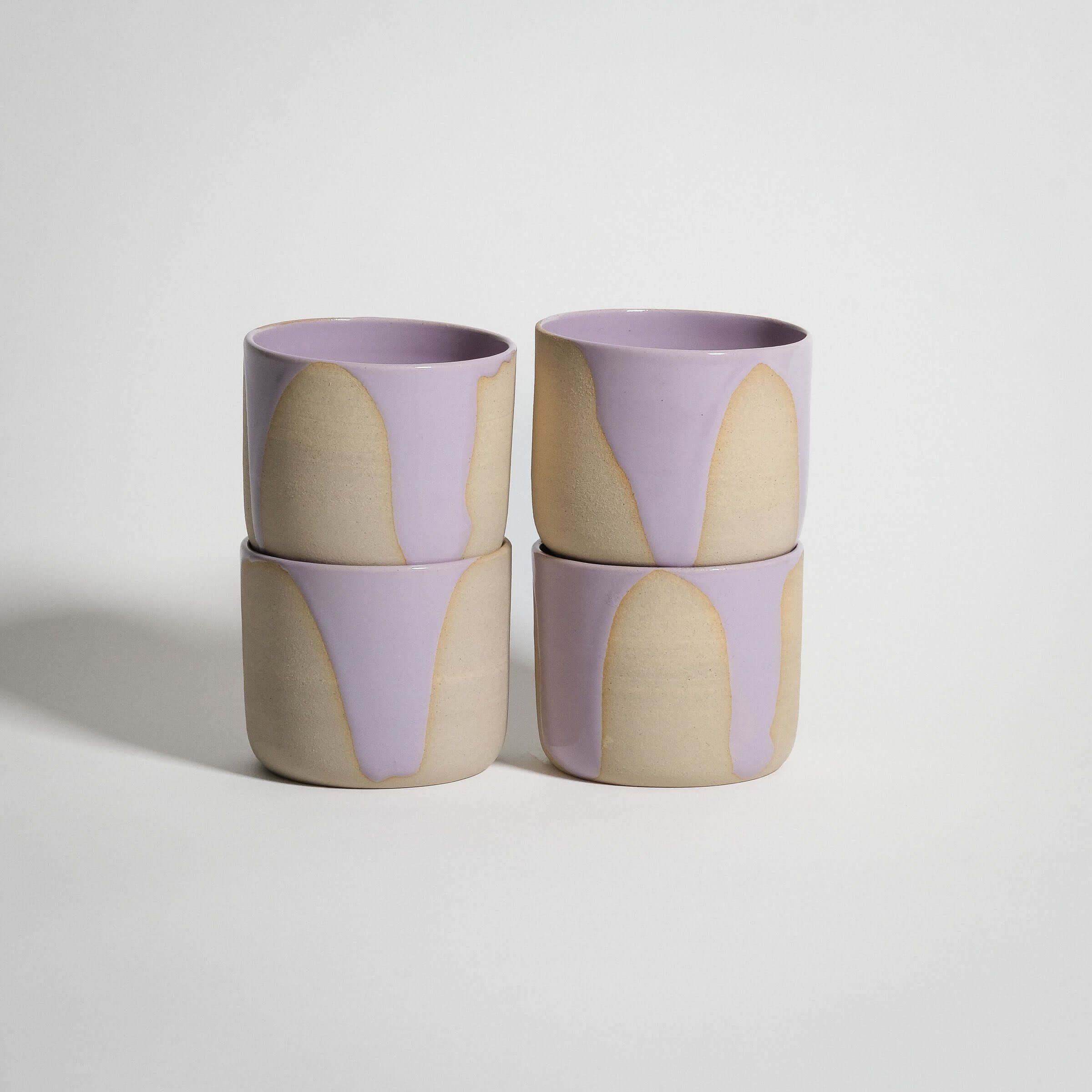 Handcrafted wheel-thrown stoneware coffee cups in lilac and pink glazes, stacked four high.