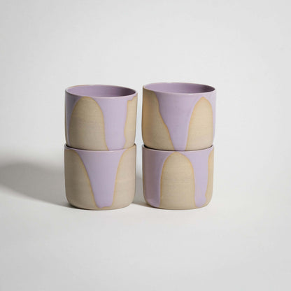 Handcrafted wheel-thrown stoneware coffee cups in lilac and pink glazes, stacked four high.