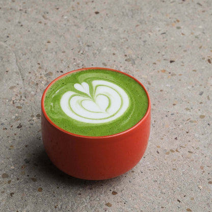 Matcha cup in glossy red glaze with latte art on creamy green matcha drink, ideal for iced beverages or artistic presentations.