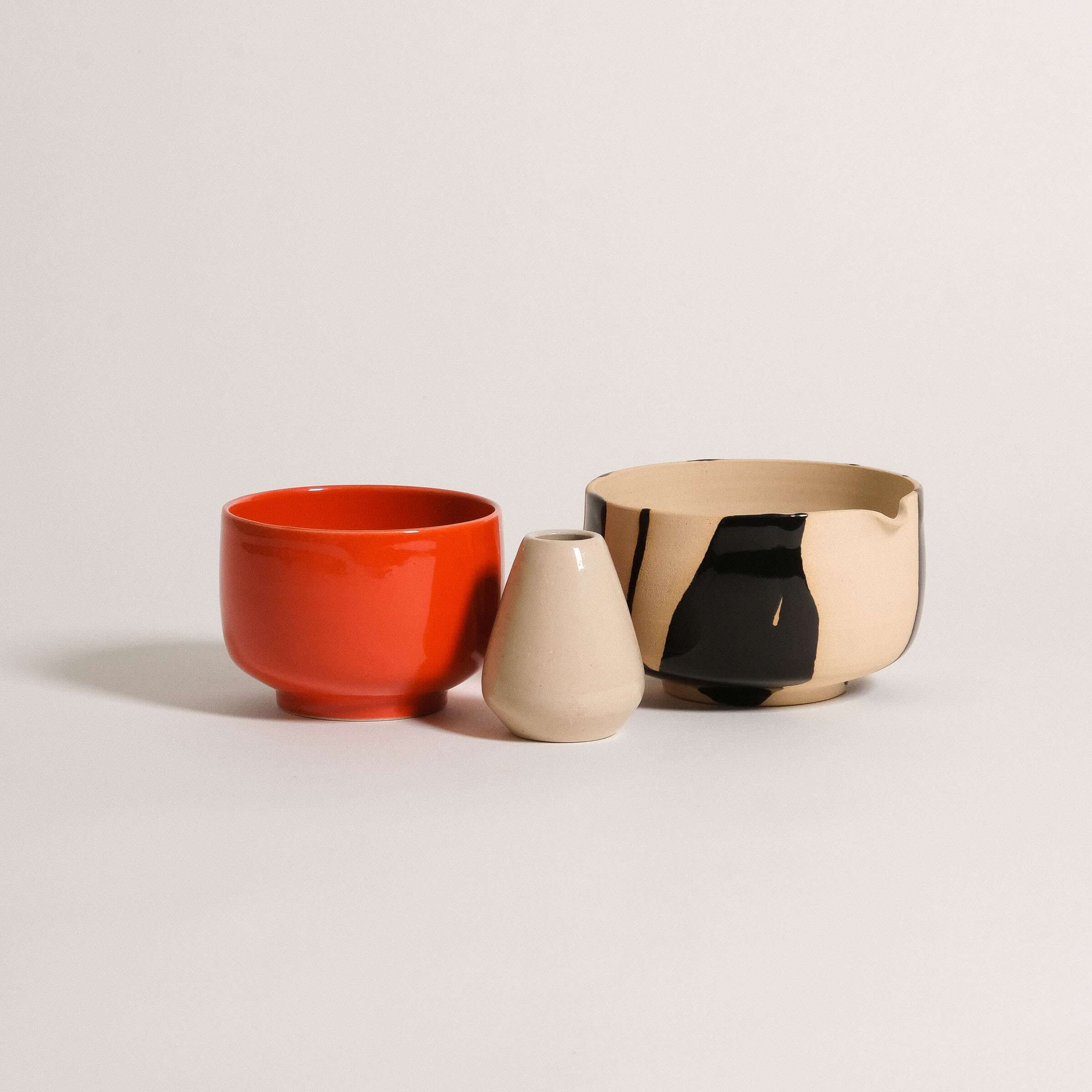 Set of three handcrafted ceramic bowls in red, beige, and black, perfect for serving snacks or decorative display.