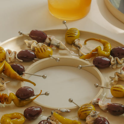 Handgefertigtes Tapas-Tablett mit Oliven und eingelegtem Gemüse auf hellem Hintergrund.