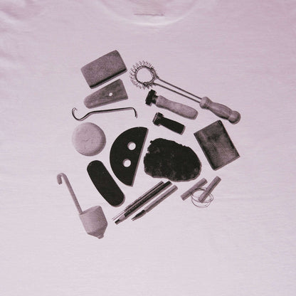 Arranged pottery tools graphic design on a lilac t-shirt, featuring various pottery implements.