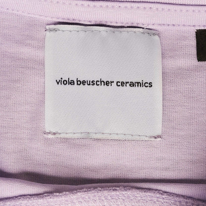 Label showing "viola beuscher ceramics" on lilac T-shirt fabric.