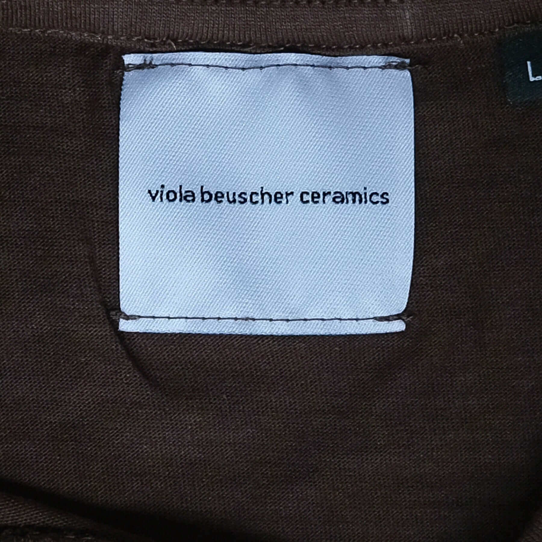 Label of vbc Team Shirt in chocolate color, featuring 'viola beuscher ceramics' text on a fabric tag.