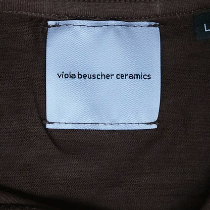 Label of vbc Team Shirt in chocolate color, featuring 'viola beuscher ceramics' text on a fabric tag.