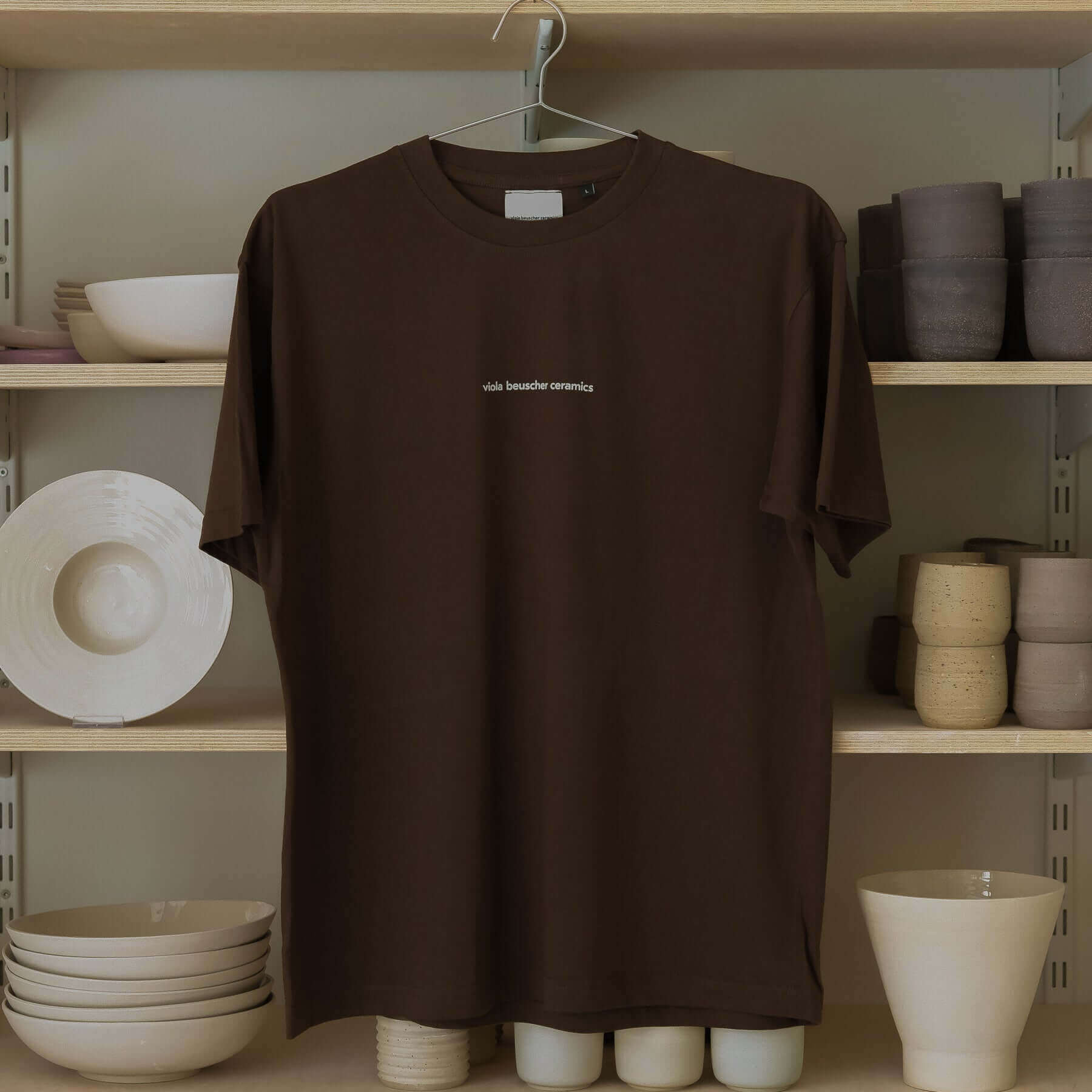 Chocolate vbc Team Shirt hanging, featuring subtle logo print and pottery tools design in a stylish setting.