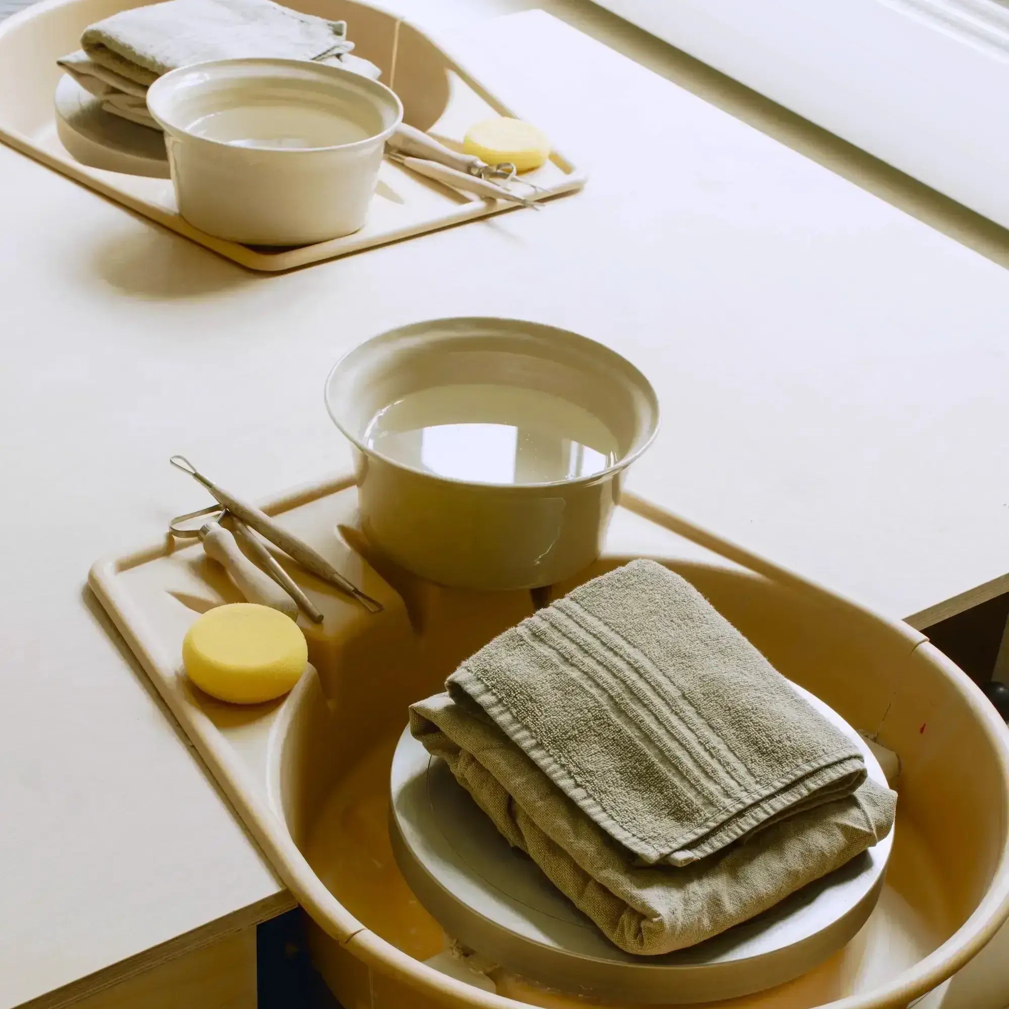 Setup for a clay class with water, sponges, and towels organized on work trays.