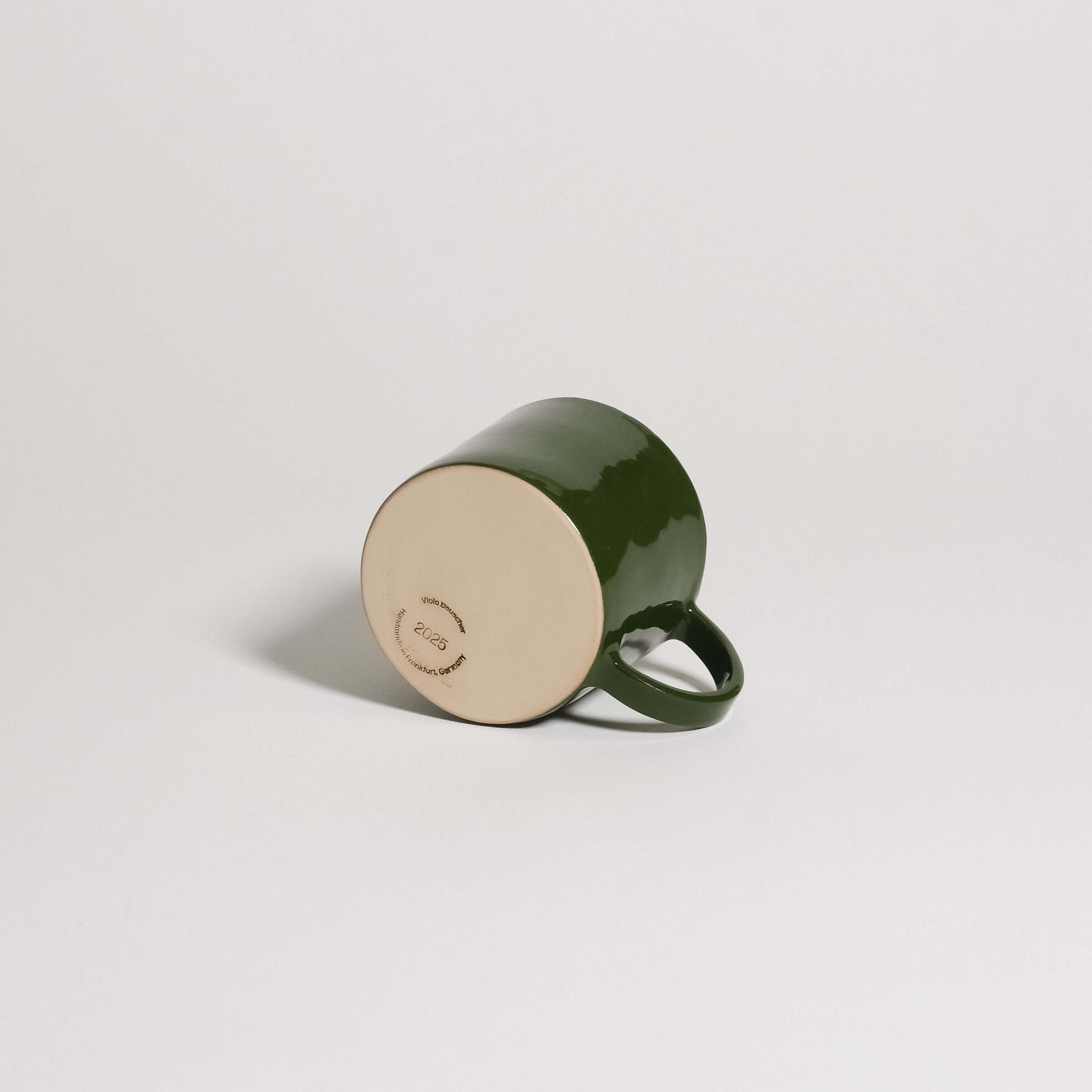 Coffee Mug – Green with glossy finish and rounded handle, showcasing the underside design in stoneware clay.