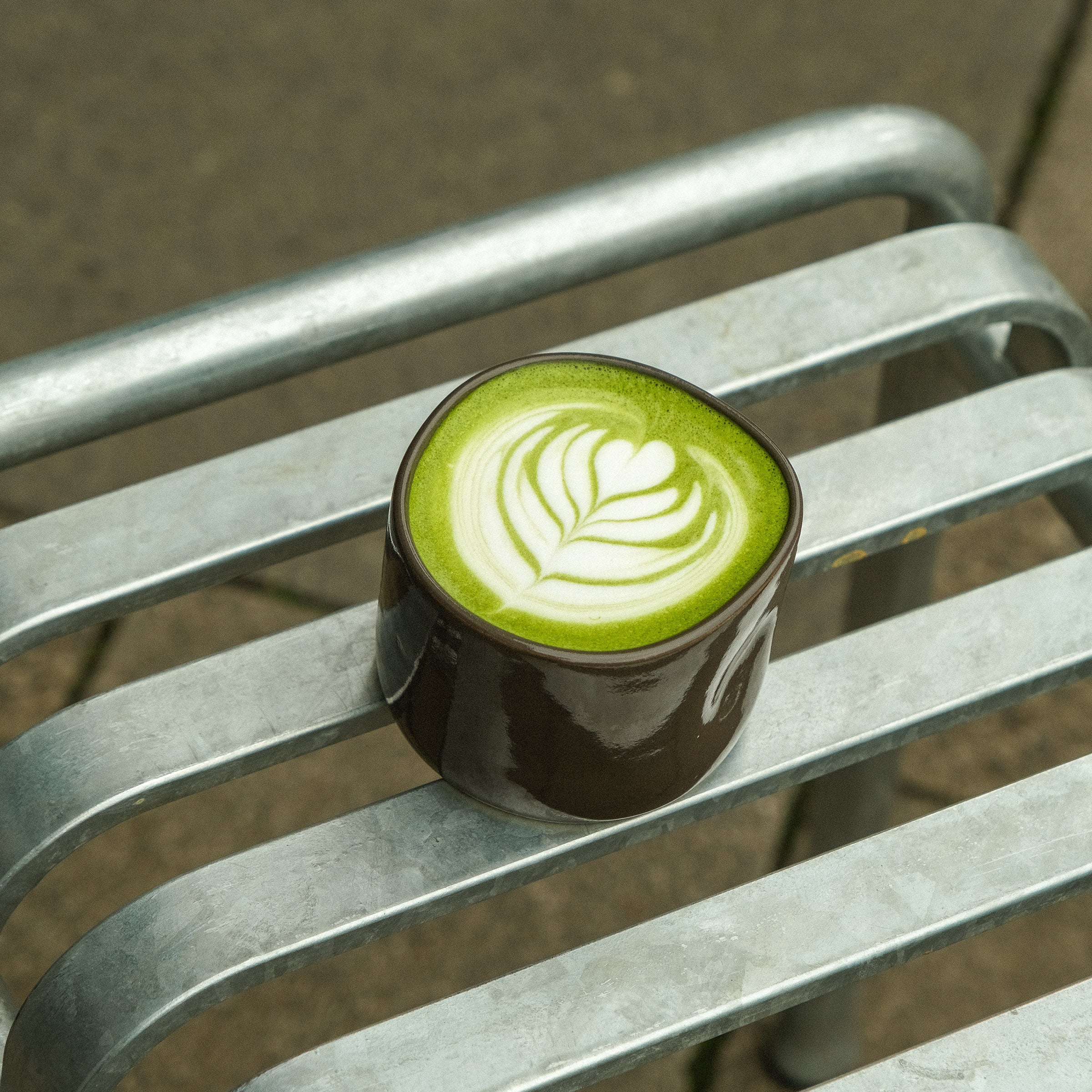 Hojicha Cup – Brown filled with green beverage on a metal bench.