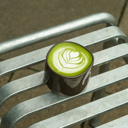 Hojicha Cup – Brown filled with green beverage on a metal bench.