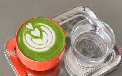 Matcha Set – Classic - Organic Ceremonial Matcha Supreme displayed with latte art in an orange cup and a glass of water.