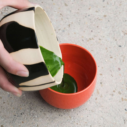 Pouring organic ceremonial matcha supreme from bowl to glossy red cup in Matcha Set – Classic - Organic Ceremonial Matcha Supreme.
