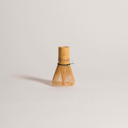 Classic bamboo matcha whisk with black thread and smiley logo for perfect foamy matcha preparation.
