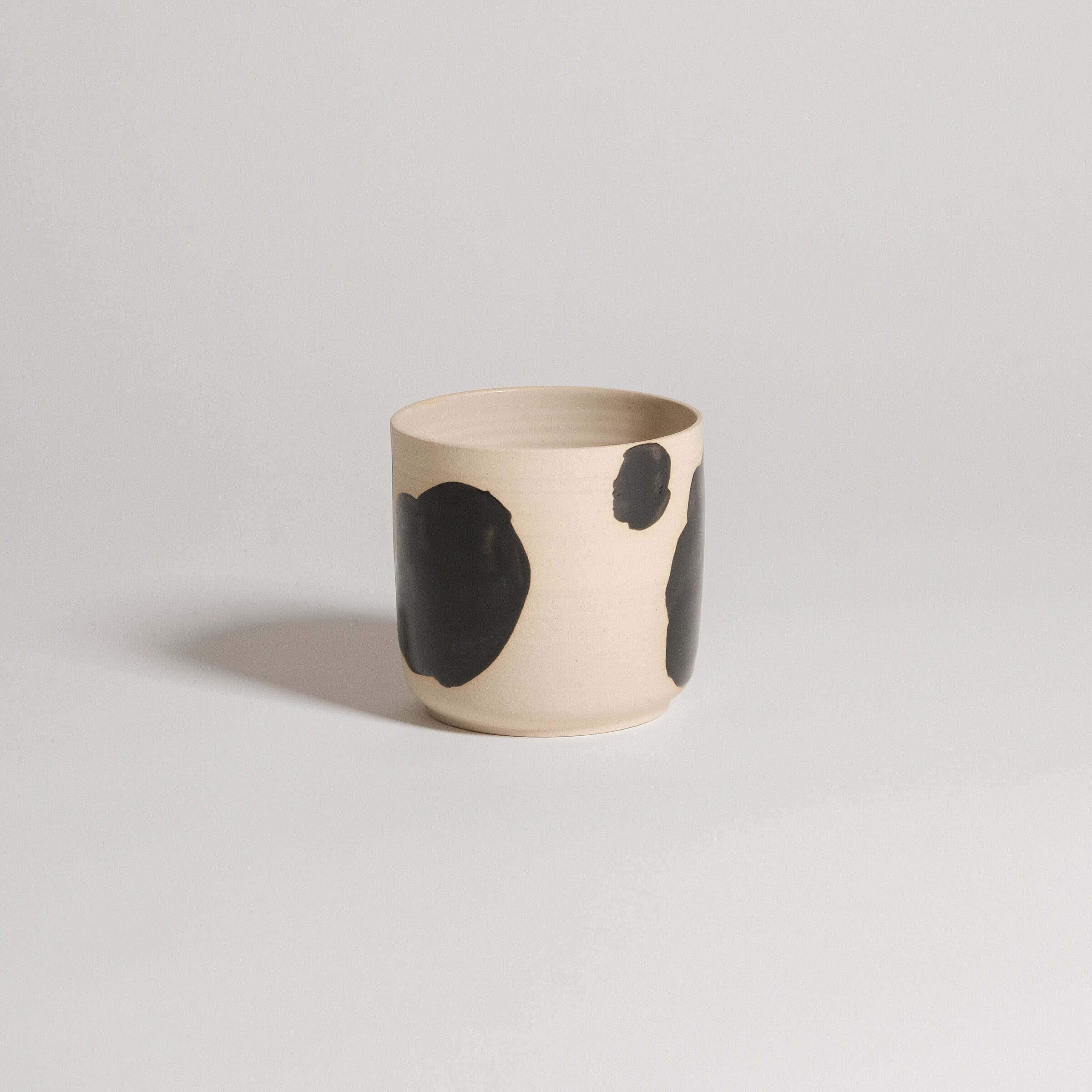 Handcrafted stoneware cup with black brush strokes, showcasing a unique design and glossy finish.