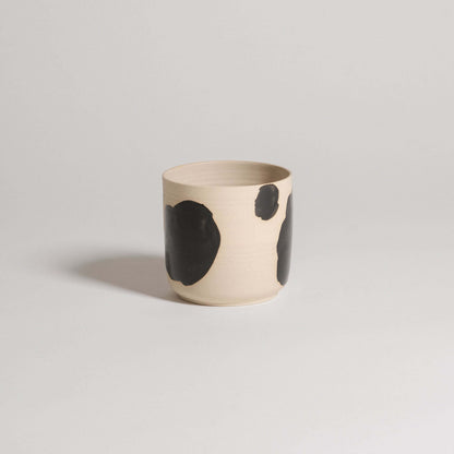 Handcrafted stoneware cup with black brush strokes, showcasing a unique design and glossy finish.