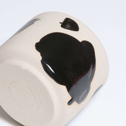 Close-up of a wheel-thrown grey stoneware cup with glossy black brush strokes and a clear glazed interior.