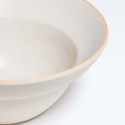 Close-up of a Neo Bowl in white matte finish with an orange rim, crafted from grey stoneware.