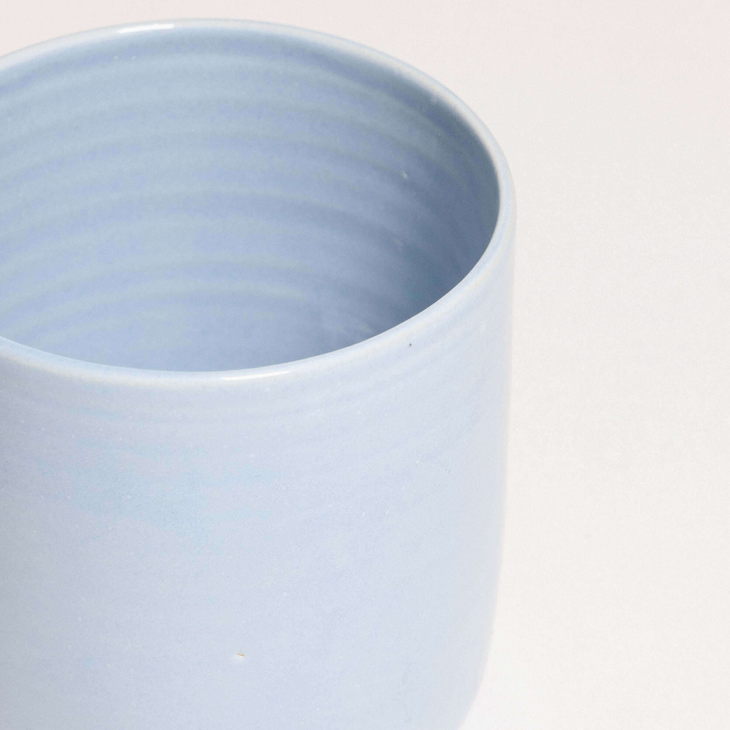 Handcrafted iceblue tea cup, Nomi design, stoneware ceramic, showcasing unique glaze and durable construction.