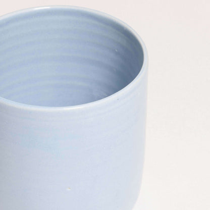 Handcrafted iceblue tea cup, Nomi design, stoneware ceramic, showcasing unique glaze and durable construction.