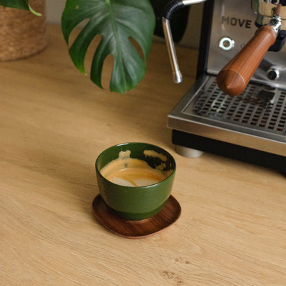 Handcrafted Yun green coffee cup from stoneware ceramic with espresso, placed on a wooden saucer.
